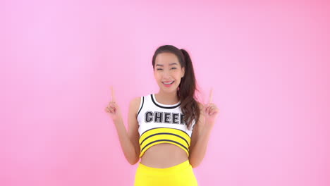 Glückliche-Asiatische-Vorbildliche-Cheerleaderin,-Die-Mit-Den-Fingern-Auf-Rosa-Aufwirft
