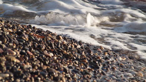 Sea-beach-of-pebbles-washed-by-foam-waves-in-slow-motion,-static,-day