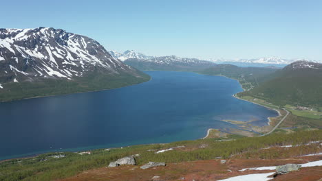 Luftaufnahme-Eines-Mannes,-Der-Auf-Einem-Bergvorsprung-Steht-Und-Auf-Einen-Fjord-Am-Arktischen-Ozean-Hinunterschaut,-Sonniger-Sommertag,-In-Rotsund,-Troms,-Nordland,-Norwegen---Dolly,-Drohnenaufnahme