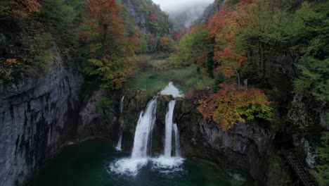 Dreamy-turquoise-waterfall-pool-in-eerie-autumn-valley,-Plitvice,-aerial