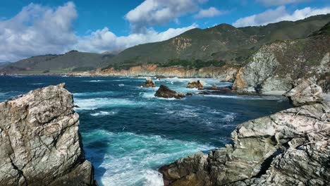 Aerial-shot-of-blue-waves-crashing-on-rocks-along-Big-Sur,-Carmel-California