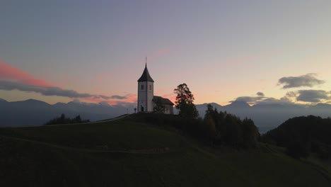 Kleine-Idyllische-Kirche-Auf-Einem-Hügel-Bei-Sonnenaufgang-In-Den-Julianischen-Alpen,-Antenne