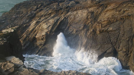 Waves-Crashing-and-Blowhole-Explodes-In-Rocky-Coastal-Landscape,-Porth-Island,-Newquay,-Cornwall,-United-Kingdom---wide-shot