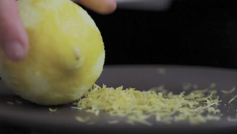 Peel-lemon-little-pieces-left-on-the-plate-after-been-grated-at-the-kitchen-table-while-cooking-tasty-pie-close-up-detail-shot