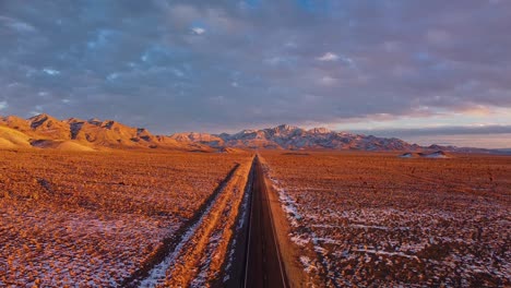 4K-aerial-of-drone-ascending-over-extraterrestrial-highway-near-Rachel-Nevada-showing-Badger-Mountain-in-the-background-at-golden-hour-with-snow-on-the-ground-and-clouds-in-the-sky