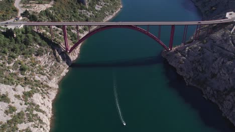 Boat-passing-under-red-Maslenica-bridge-going-through-Novsko-Zdrilo-sea-strait,-aerial