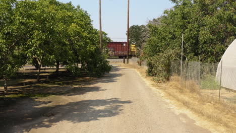 POV-shot-over-a-narrow-gravel-pathway-with-the-view-of-white-greenhouse-building-on-right-side-and-a-goods-train-passing-by-in-the-front-on-a-sunny-day
