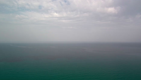 High-aerial-descending-flight-above-vast-green-ocean-salt-water-sea-on-cloudy-and-hazy-day