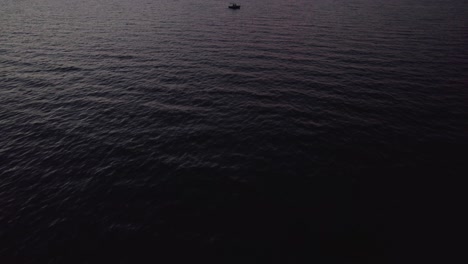 Small-leisure-boat-floating-in-dark-sea-during-nightfall,-aerial