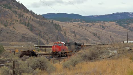 Pan-shot-of-a-red-train-waiting-on-the-railway-in-a-scenic-desert-environment-close-to-Sovana,-Kamloops,-British-Columbia-,Canada