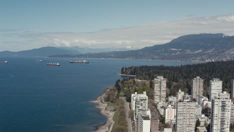 Aerial-fly-over-English-Bay-second-beach-stanley-park-residential-beachside-park-road-as-freightors-are-in-the-harbor-fueling-up-exports-imports-on-hot-summer-day-suprinsingly-quiet-traffic-and-people