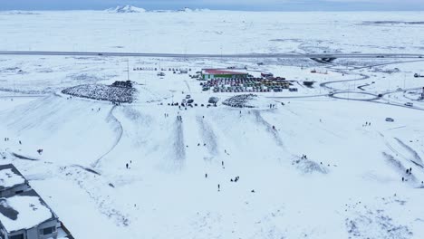 Local-Iceland-people-enjoying-white-snow-winter-fun-sliding-down-hill-on-sleds,-aerial