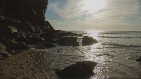 Water-pours-over-rocks-as-tide-rolls-into-Chapel-Porth-beach-at-sunset,-wide