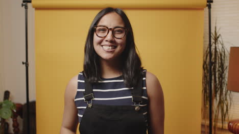 Happy-young-Asian-woman-holds-peace-sign-up-to-the-camera-in-a-yellow-studio
