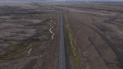 Car-drives-on-Hringvegur-ring-road-immense-vast-open-volcanic-moss-landscape,-aerial
