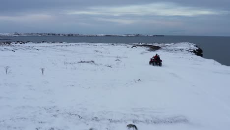 Person-on-atv-quad-bike-riding-along-rugged-snow-covered-coastal-cliffs-in-Iceland