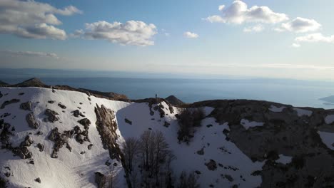 Hiker-alone-on-top-of-snowy-ridge-looking-to-the-sea,-Sveti-Jure-mountains-,-Biokovo,-Croatia