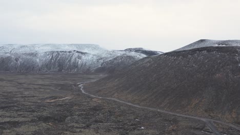 Rugged-terrain-in-Iceland-highlands-with-remote-road-below-mountain-slope,-aerial