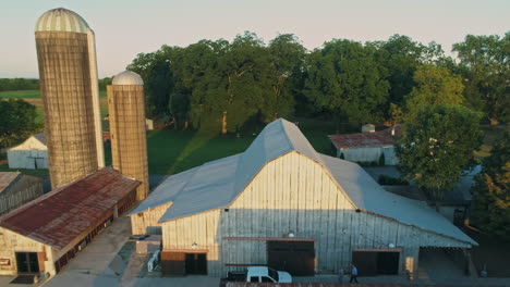 Aerial-passing-closely-over-top-of-barn-revealing-grain-silos-on-farm,-4K