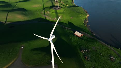 High-Angle-above-Wind-Turbine-propeller-spinning-on-Rural-green-hills-with-Red-barn-along-river,-Montezuma-hills,-California