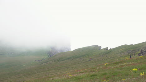 Hikers-climbing-on-grassy-cliff-with-foggy-view,-Iceland