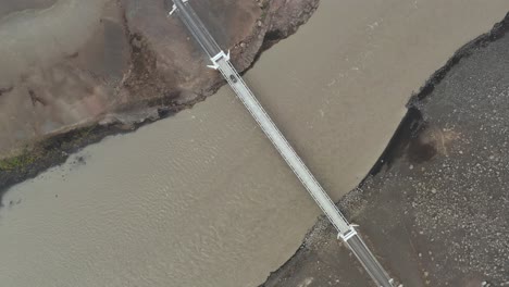 Above-bridge-in-Iceland-crossing-brown-glacial-river,-remote-highlands,-aerial