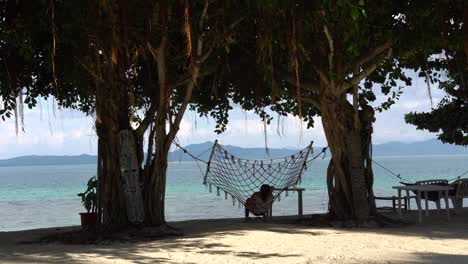 Woman-Resting-On-A-Net-Hammock-Under-The-Shady-Trees-In-Dos-Palmas-Island-Resort-In-Puerto-Princesa,-Palawan,-Philippines---Medium-Shot