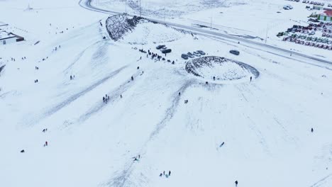 Aerial-view-of-people-enjoying-snowy-hill-for-sledding-during-winter-time