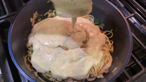 Pouring-a-jar-of-white-and-creamy-Alfredo-sauce-over-cooked-pasta-noodles-with-sauteed-vegetables