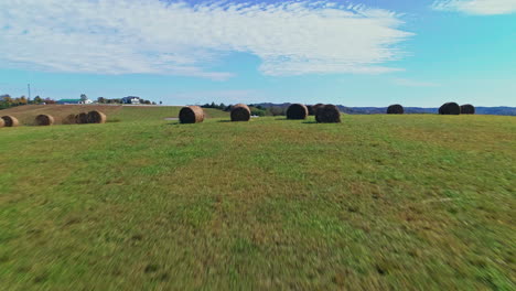 Aerial-passing-over-hay-bales-on-hill-to-reveal-scenic-rural-countryside,-4K