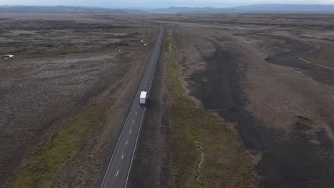 Truck-driving-endless-road-in-flat-volcanic-Iceland-landscape,-Hringvegur-ring-road,-aerial