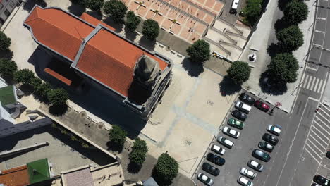 Aufnahme-Von-Oben-Nach-Unten-Der-Kirche-Sao-Bento-De-Porta-Aberta-In-Portugal-Mit-Autos,-Die-Bei-Heißem,-Sonnigem-Wetter-Auf-Dem-Vorderen-Parkplatz-Geparkt-Sind---Antenne