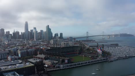 Descending-aerial-shot-of-Oracle-Park-with-the-San-Francisco-skyline-in-the-background-on-a-foggy-day