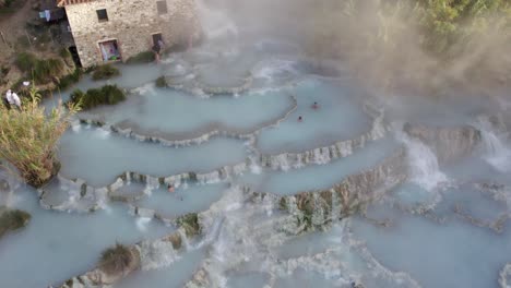 Unique-blue-waterfall-pools-at-Saturnia-hot-spring,-people-relaxing-in-hot-water,-aerial