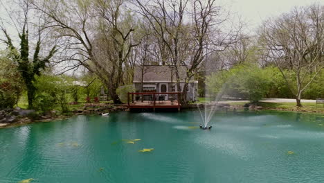 Aerial-view-of-private-cottage-with-deck-overlooking-blue-pond-with-fountain