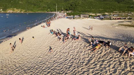 Aerial-drone-scene-with-beach-and-people-enjoying-the-sunset-on-the-dunes-and-having-fun-in-the-sand-on-top-of-the-dunes-of-Florianópolis-Brazil