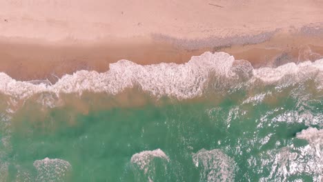 Statische-Luftaufnahme-Von-Atemberaubenden-Meergrünen-Wellen,-Die-Gegen-Einen-Rosafarbenen-Sandstrand-Schlagen