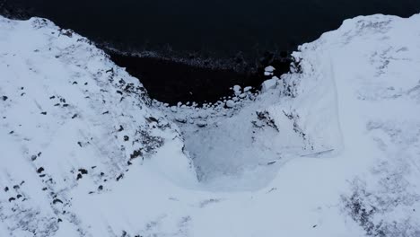 Steep-rocky-cliffs-covered-in-snow-during-winter-time,-Iceland,-aerial