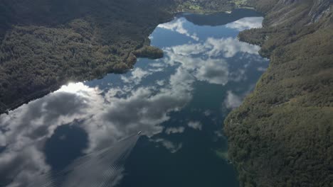 Lago-Bohinj-Con-Un-Impresionante-Reflejo-Del-Cielo-En-La-Superficie,-Barco-Que-Viaja-En-El-Agua,-Aéreo