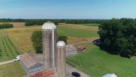 Aerial-orbiting-grain-silos-on-rural-farm-with-crop-fields-in-background,-4K