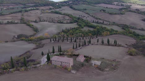 Tuscany-old-rural-estate-on-hilltop-with-iconic-road-and-cypress-trees,-aerial