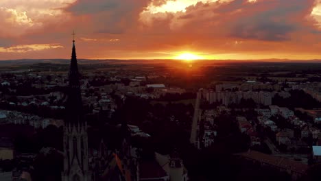 Rotating-aerial-view-of-the-Olomouc-city-of-Czech-Republic,-showing-church-tower-against-red-sun-in-city-during-sunset