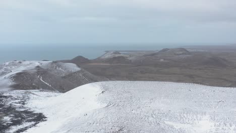 Snow-covered-mountains-during-winter-in-Iceland-with-view-of-distant-Atlantic-Ocean,-aerial