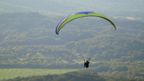 Paragliding-soaring-through-the-air,-solo-paraglider-floats-peacefully-in-slow-motion