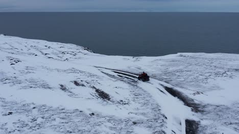 Adventurer-on-quad-bike-reaching-Njarðvík-coastline-during-winter,-aerial