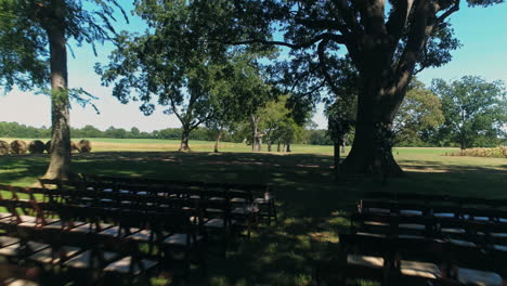 Aerial-passing-low-over-wedding-alter-under-large-trees-at-venue,-4K