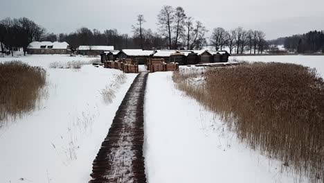 Historic-Dwelling-Houses-Covered-With-Snow-During-Winter-In-Araishi-Archaeological-Park-In-Latvia