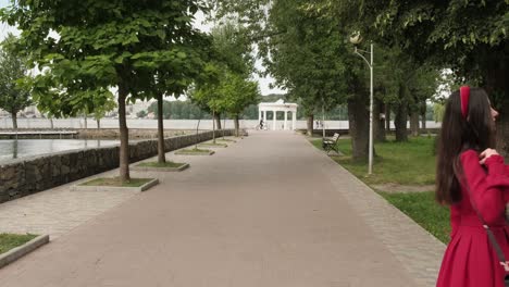 Wunderschöne-Brünette-In-Rot-Geht-Im-Park-In-Der-Nähe-Des-Sees-Spazieren
