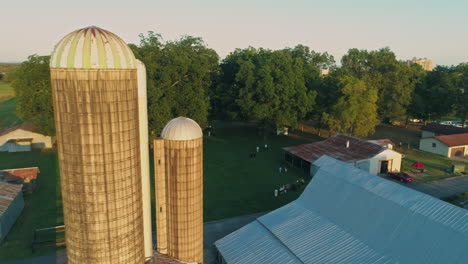 Aerial-orbiting-closely-to-large-grain-silos-on-farm-with-barn-and-trees,-4K