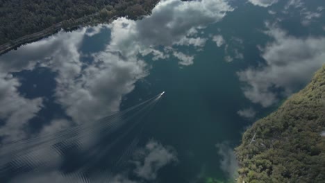 Clouds-and-sky-reflecting-on-smooth-water-surface-of-lake-with-boat-creating-ripples,-aerial